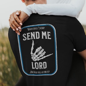 Puede incluir: Camiseta negra con un dise&ntilde;o rectangular blanco y azul en la espalda. El dise&ntilde;o incluye el texto "WHOM SHALL I SEND? SEND ME LORD AND WHO WILL GO FOR US?" y una mano de esqueleto blanca.