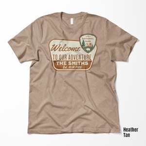Puede incluir: Una camiseta de color marr&oacute;n claro con un cartel de parque nacional vintage de color marr&oacute;n y verde que dice "Bienvenido a nuestra aventura The Smiths Est. 10.01.2025".