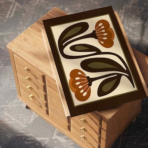 Puede incluir: Una impresi&oacute;n art&iacute;stica enmarcada con un dise&ntilde;o floral retro. La impresi&oacute;n presenta flores marrones y naranjas y hojas verdes sobre un fondo crema. Se muestra sobre una c&oacute;moda de madera con pomos dorados. La obra de arte tiene un borde marr&oacute;n oscuro.