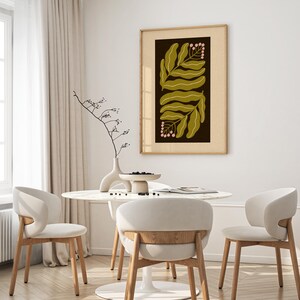 Pu&ograve; includere: Una stampa botanica incorniciata con foglie verde oliva e bacche rosa su sfondo marrone scuro. L'opera d'arte &egrave; in una cornice di legno chiaro. L'immagine &egrave; in una sala da pranzo con un tavolo rotondo e sedie bianche.
