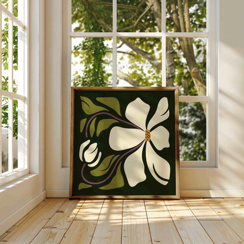 May include: Framed art print depicting a stylized white magnolia flower with a yellow centre and purple stems against a dark green backdrop. The artwork is displayed in a room with natural light from a window.