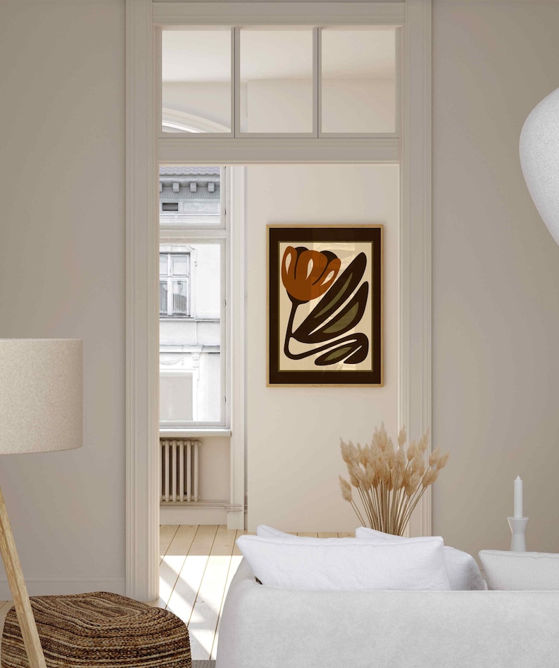 K&ouml;nnte beinhalten: Ein abstrakter Kunstdruck mit einem braunen Tulpendesign mit gr&uuml;nen Bl&auml;ttern auf cremefarbenem Hintergrund, gerahmt in einem dunkelbraunen Holzrahmen. Das Kunstwerk h&auml;ngt an einer cremefarbenen Wand in einem Raum mit einem wei&szlig;en Sofa und einer Stehlampe.