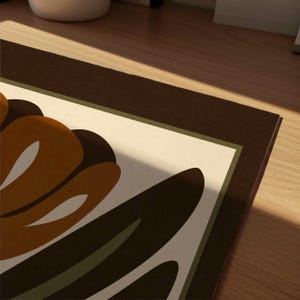 K&ouml;nnte beinhalten: Ein dekorativer Kunstdruck mit einem stilisierten Blumendesign. Das Kunstwerk zeigt eine warme Farbpalette mit Braunt&ouml;nen, Beige und Olivgr&uuml;n. Der Druck hat einen dunkelbraunen Rand und ist vor einem hellen Hintergrund platziert.