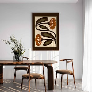 Puede incluir: Un cuadro enmarcado con dos flores estilizadas en tonos marr&oacute;n y naranja sobre un fondo crema. La obra de arte se presenta en un marco de madera marr&oacute;n oscuro, ideal para la decoraci&oacute;n del hogar.