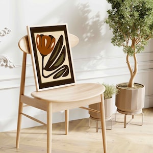 K&ouml;nnte beinhalten: Ein gerahmter Kunstdruck mit einem stilisierten Blumendesign in Braun-, Olivgr&uuml;n- und Beiget&ouml;nen. Das Kunstwerk wird auf einem hellen Holzstuhl pr&auml;sentiert, mit einer Topfpflanze im Hintergrund. Der Stil ist modern und minimalistisch.