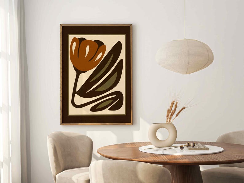 K&ouml;nnte beinhalten: Gerahmter Kunstdruck mit einer stilisierten Blume in Braun-, Olivgr&uuml;n- und Beiget&ouml;nen. Das Kunstwerk wird in einem dunkelbraunen Holzrahmen pr&auml;sentiert. Das Bild ist Teil einer Wohnkultur, mit einem runden Holztisch und St&uuml;hlen.