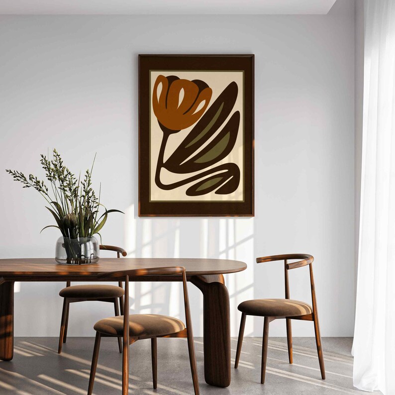 K&ouml;nnte beinhalten: Ein gerahmter Kunstdruck mit einer stilisierten Blume in Braun- und Olivgr&uuml;nt&ouml;nen auf cremefarbenem Hintergrund. Das Kunstwerk h&auml;ngt an einer wei&szlig;en Wand &uuml;ber einem Esstisch und St&uuml;hlen aus Holz und schafft ein modernes Interieur.