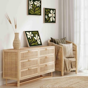May include: Three framed floral art prints with white flowers and green leaves hang on a white wall. A woven wood dresser with six drawers and a vase with wheat stalks sit below the art. A woven chair and a round jute rug complete the room.