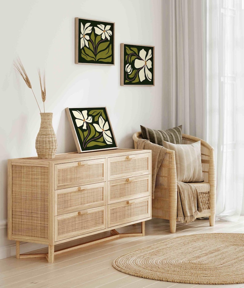 May include: Three framed floral art prints with white flowers and green leaves hang on a white wall. A woven wood dresser with six drawers and a vase with wheat stalks sit below the art. A woven chair and a round jute rug complete the room.