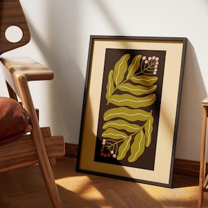 Pu&ograve; includere: Stampa artistica incorniciata con un design botanico. L'opera presenta due grandi foglie verde oliva e piccoli grappoli di bacche rosa su uno sfondo marrone scuro. La stampa &egrave; in una cornice nera, appoggiata a un muro.