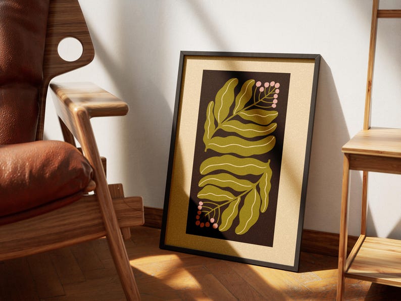 Pu&ograve; includere: Stampa artistica incorniciata con un design botanico. L'opera presenta due grandi foglie verde oliva e piccoli grappoli di bacche rosa su uno sfondo marrone scuro. La stampa &egrave; in una cornice nera, appoggiata a un muro.