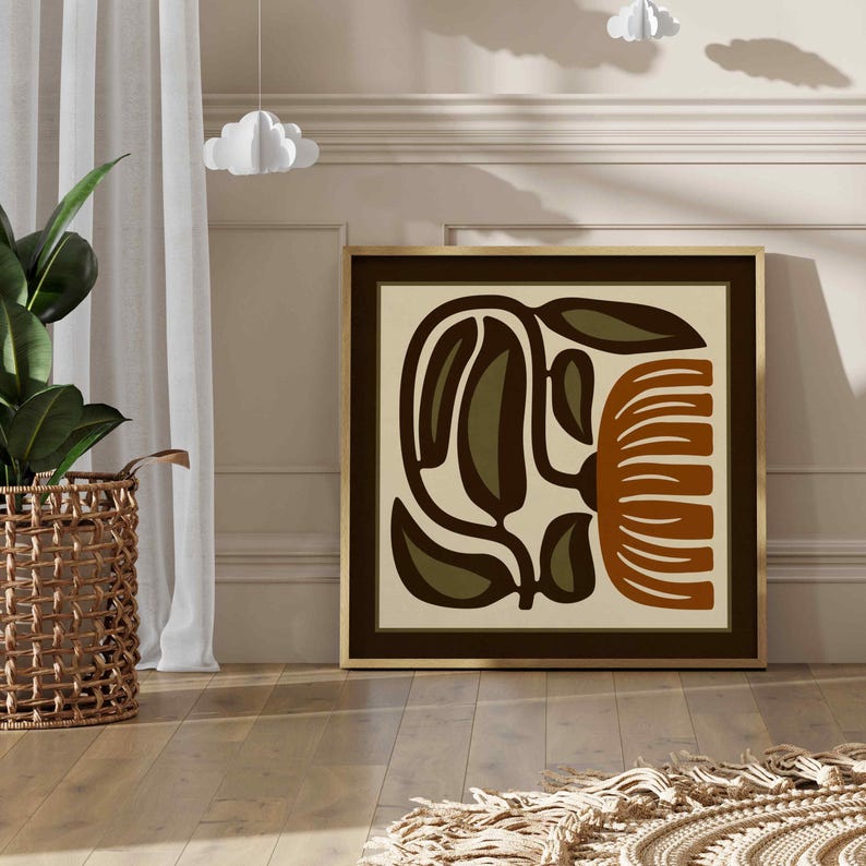 May include: A framed abstract art print with a botanical design in brown, olive green, and cream. The artwork has a dark brown border and a gold frame. The print is displayed on a light-coloured wall.