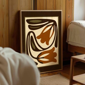 May include: A framed abstract art print featuring a floral design in shades of brown, olive green, and cream. The artwork is displayed in a room with wooden paneling and a bed, suggesting a home decor theme.