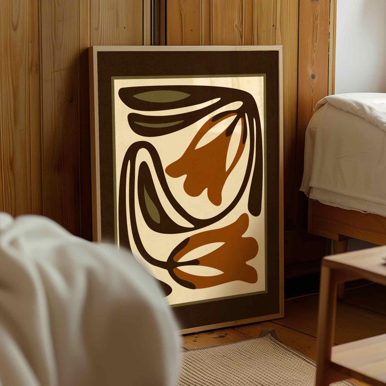 May include: A framed abstract art print featuring a floral design in shades of brown, olive green, and cream. The artwork is displayed in a room with wooden paneling and a bed, suggesting a home decor theme.
