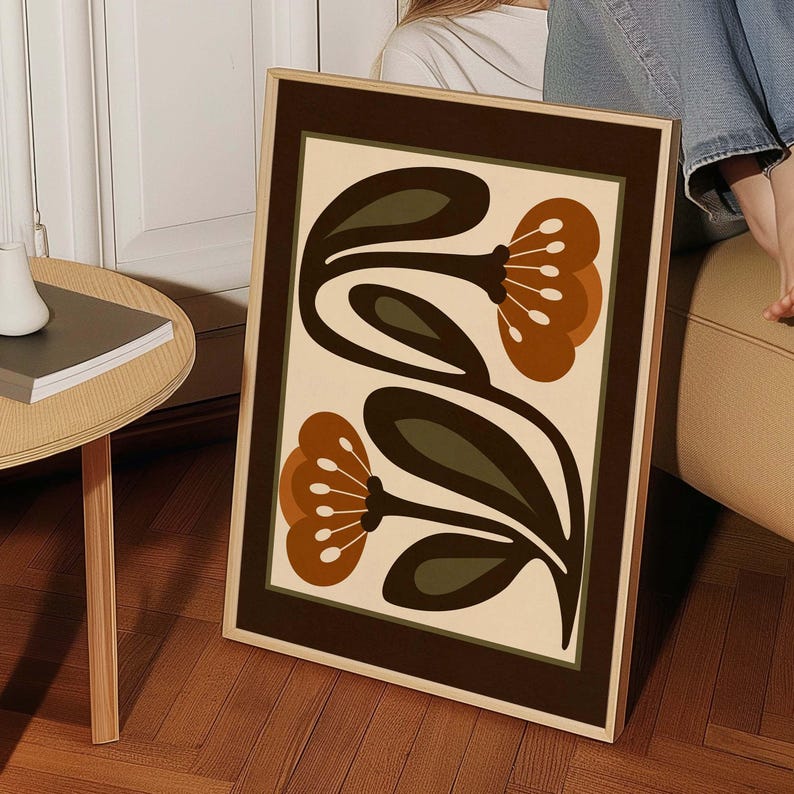 Puede incluir: L&aacute;mina art&iacute;stica enmarcada con un dise&ntilde;o floral. La obra presenta dos grandes flores con p&eacute;talos marrones y hojas verde oscuro sobre un fondo crema. La impresi&oacute;n est&aacute; enmarcada con un borde marr&oacute;n y un marco de madera clara.