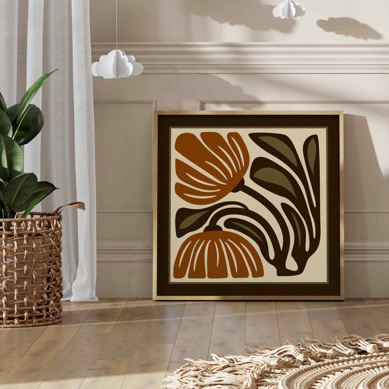 May include: A framed art print featuring stylized orange and brown flowers with green leaves against a cream background. The artwork is in a dark brown frame and is displayed on a wooden floor.