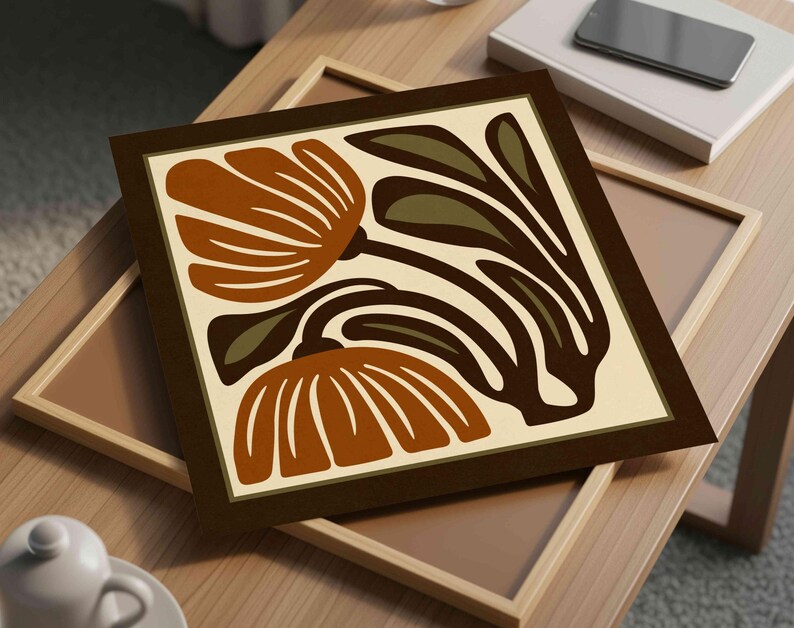 May include: A framed art print featuring a stylized floral design in shades of brown, tan, and olive green. The artwork is set against a cream background and framed in a dark brown border. The print is displayed on a wooden surface.