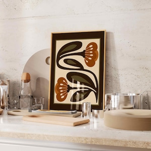 Puede incluir: Un cuadro enmarcado con un dise&ntilde;o floral estilizado. La obra de arte muestra dos flores grandes en tonos marrones y naranjas, con hojas verdes, sobre un fondo crema. El marco es de color marr&oacute;n oscuro.