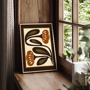 Puede incluir: Una impresi&oacute;n art&iacute;stica enmarcada con un dise&ntilde;o floral. La impresi&oacute;n presenta dos flores estilizadas en tonos marrones y naranjas sobre un fondo crema. Se exhibe en un alf&eacute;izar de madera, con una ventana y una cortina en el fondo.