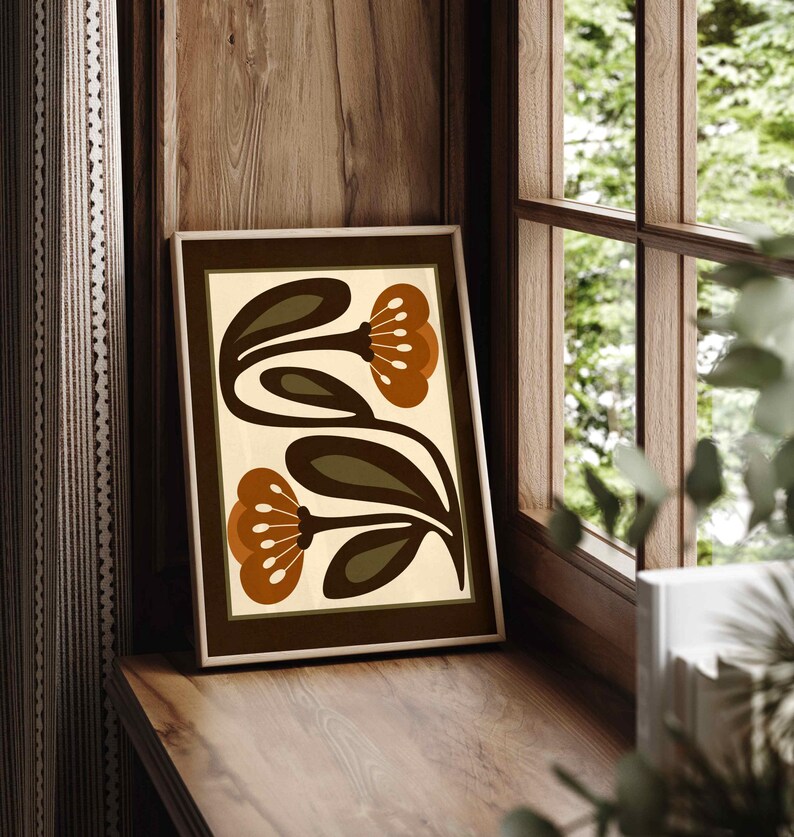 Puede incluir: Una impresi&oacute;n art&iacute;stica enmarcada con un dise&ntilde;o floral. La impresi&oacute;n presenta dos flores estilizadas en tonos marrones y naranjas sobre un fondo crema. Se exhibe en un alf&eacute;izar de madera, con una ventana y una cortina en el fondo.