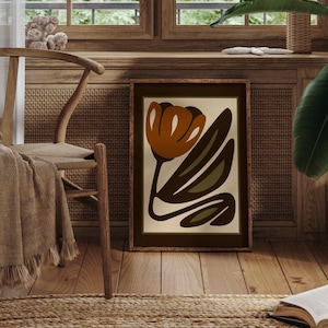 K&ouml;nnte beinhalten: Ein gerahmter Kunstdruck mit einem abstrakten Blumendesign in Braun-, Orange- und Gr&uuml;nt&ouml;nen. Das Kunstwerk steht auf einem Holzboden, gelehnt an einer Wand. Ein Holzstuhl mit einer Decke und einem Teppich befinden sich im Vordergrund.