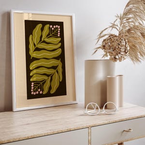 Pu&ograve; includere: Una stampa botanica incorniciata con un bordo bianco. L'opera presenta foglie verde oliva e bacche rosa su uno sfondo scuro. La stampa &egrave; esposta su una scrivania in legno chiaro con vasi decorativi e occhiali.
