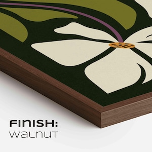 May include: A framed art print with a large white flower, yellow center, and green leaves on a dark green backdrop. The frame is dark walnut. The text "FINISH: WALNUT" is visible. The artwork is framed in a dark wood.