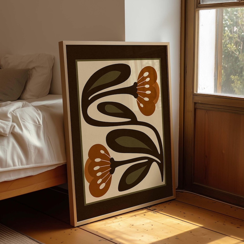 Puede incluir: L&aacute;mina art&iacute;stica floral enmarcada con un dise&ntilde;o estilizado. La obra presenta dos flores con p&eacute;talos marrones y hojas verdes sobre un fondo crema, enmarcada en un borde marr&oacute;n oscuro. La impresi&oacute;n est&aacute; sobre un suelo de madera.