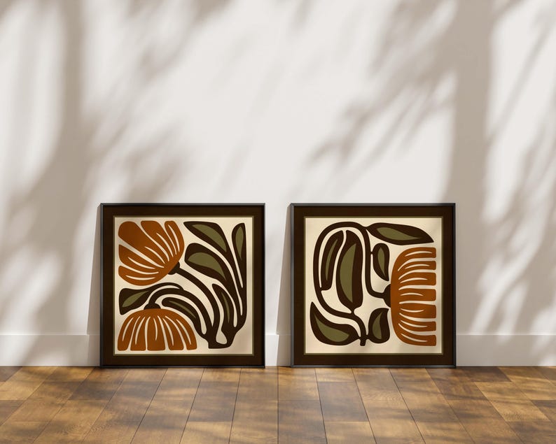 May include: Two framed art prints with abstract floral designs. Each print has a square format with a dark brown frame. The artwork features stylized flowers in shades of brown, olive green, and cream, creating a modern aesthetic.