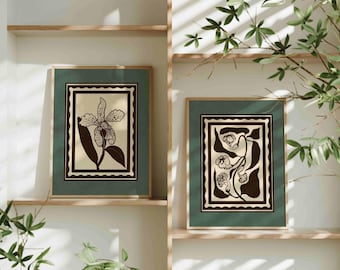 May include: Two framed botanical art prints. Each print features a floral illustration in black and beige, set against a green background. The frames are a natural wood colour, and the prints are displayed on wooden shelves.
