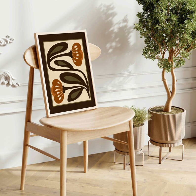 Puede incluir: Una impresi&oacute;n art&iacute;stica enmarcada con un dise&ntilde;o floral retro. La obra presenta flores y hojas marrones y verde oliva sobre un fondo crema. La impresi&oacute;n se muestra en una silla de madera clara. Una planta en maceta est&aacute; en el fondo.