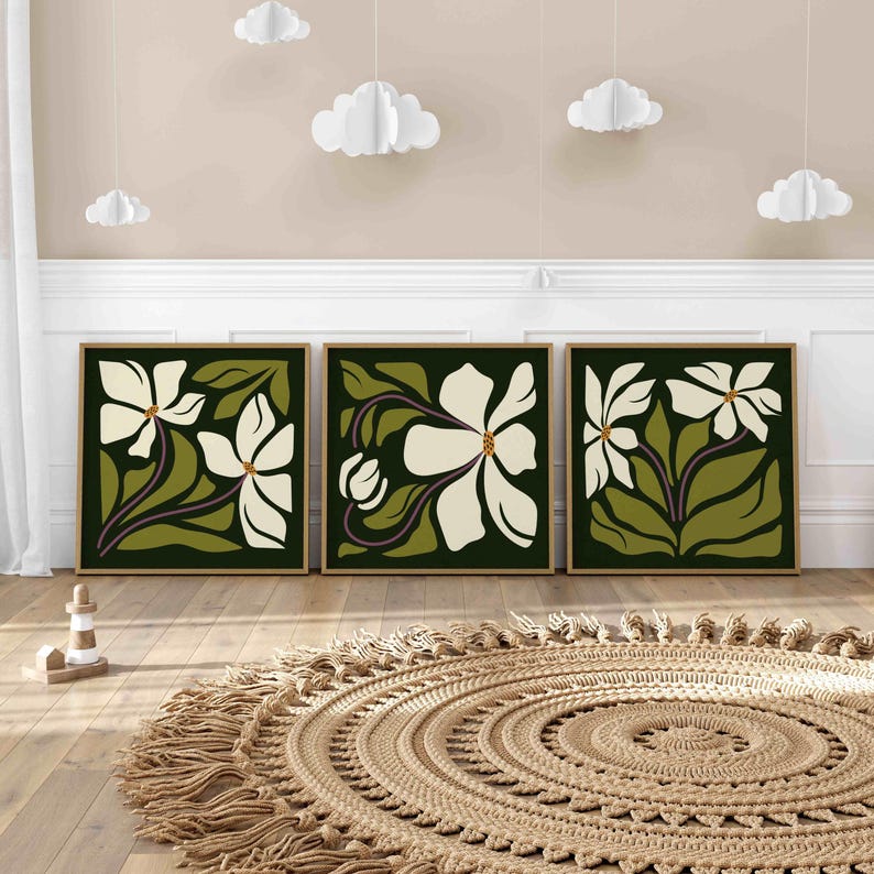 May include: Three framed floral art prints. Each print features a white flower with green leaves and purple stems against a dark green background. The frames are a light brown colour. The art is displayed above a round, woven rug.