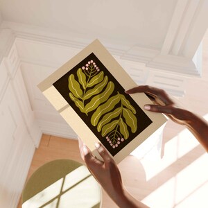 Pu&ograve; includere: Una stampa botanica incorniciata con foglie verde oliva e grappoli di bacche rosa su sfondo marrone scuro. La stampa &egrave; incorniciata in una cornice beige, creando un'estetica moderna e minimalista.