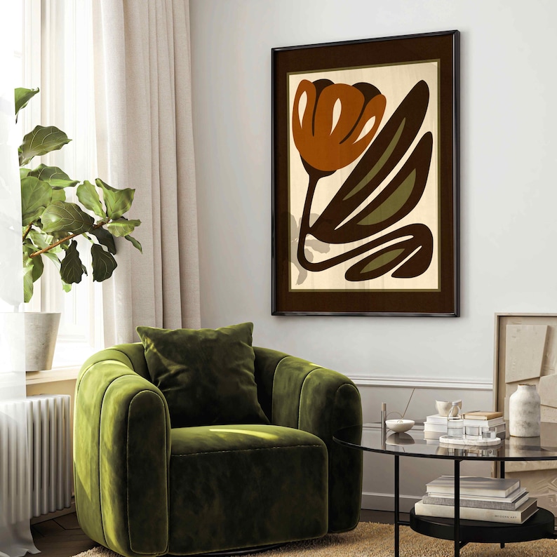 K&ouml;nnte beinhalten: Ein gerahmter Kunstdruck mit einer stilisierten orangefarbenen Blume mit braunen und gr&uuml;nen Bl&auml;ttern. Das Kunstwerk ist vor einem cremefarbenen Hintergrund platziert und in einem dunkelbraunen Rahmen eingefasst. Der Druck h&auml;ngt &uuml;ber einem gr&uuml;nen Samtsessel.