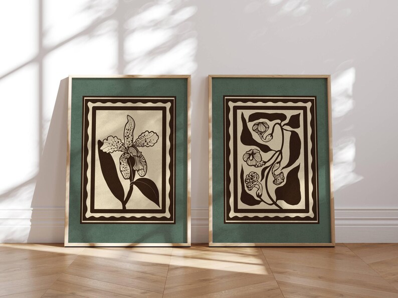 Op de afbeelding: Twee ingelijste botanische kunstprints. Elke print heeft een bloemenontwerp in zwart en beige, tegen een groene achtergrond met een gouden lijst. Het kunstwerk wordt tentoongesteld op een lichte houten vloer tegen een witte muur.