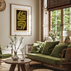 Pu&ograve; includere: Una stampa botanica incorniciata con foglie verde oliva e grappoli di bacche rosa su sfondo scuro. L'opera d'arte &egrave; in una stanza con un divano verde, mobili in legno e una tenda a rullo in tessuto. La stanza &egrave; decorata in toni neutri.