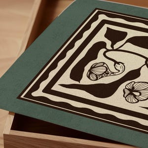 Op de afbeelding: Een rechthoekige, teal-gekleurde decoratieve mat met een beige bloemenontwerp en een donkerbruine rand. De mat bevindt zich gedeeltelijk in een houten lade, waardoor de textuur en het patroon worden benadrukt. Het bloemenontwerp omvat gestileerde bloem- en bladvormen.