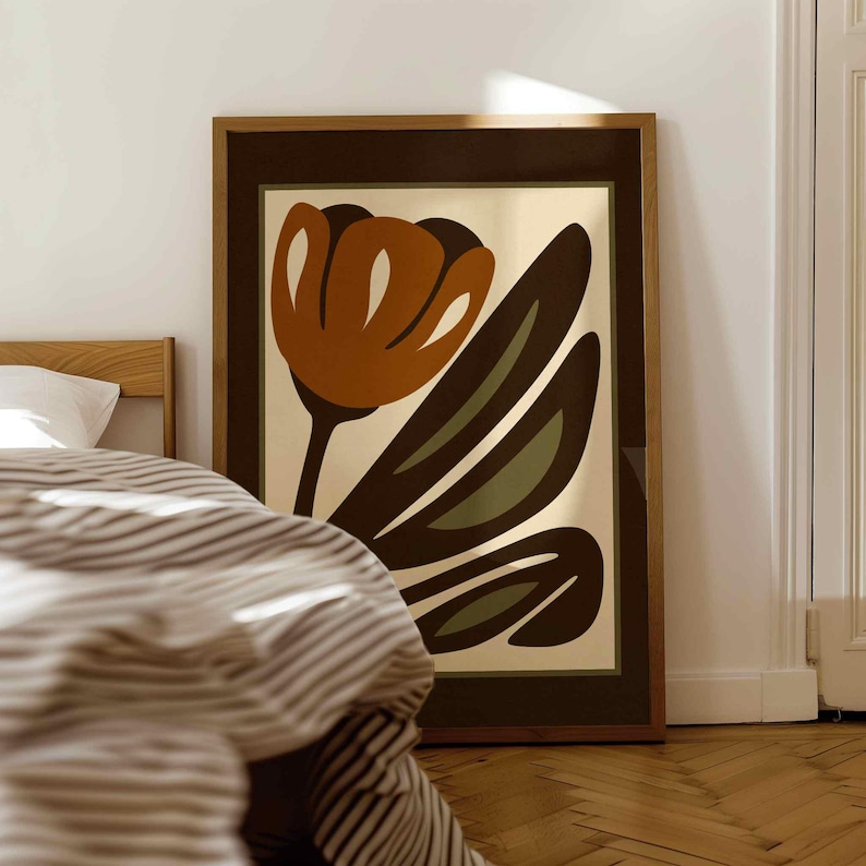 K&ouml;nnte beinhalten: Ein gerahmter Kunstdruck mit einer stilisierten Blume in Braun-, Orange- und Gr&uuml;nt&ouml;nen. Das Kunstwerk ist vor einem cremefarbenen Hintergrund platziert und in einem dunkelbraunen Holzrahmen gerahmt. Der Druck wird in einem Schlafzimmer gezeigt.