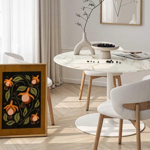 K&ouml;nnte beinhalten: Ein gerahmter Druck eines Blumendesigns mit orangefarbenen und rosafarbenen Blumen auf schwarzem Hintergrund. Der Druck h&auml;ngt an einer Wand in einem Raum mit einem wei&szlig;en Marmortisch und St&uuml;hlen.