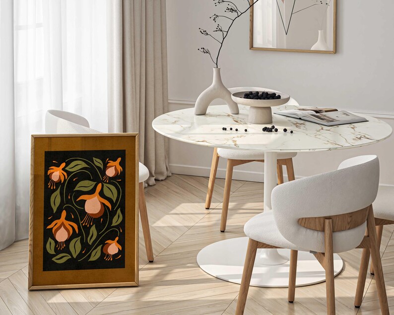 K&ouml;nnte beinhalten: Ein gerahmter Druck eines Blumendesigns mit orangefarbenen und rosafarbenen Blumen auf schwarzem Hintergrund. Der Druck h&auml;ngt an einer Wand in einem Raum mit einem wei&szlig;en Marmortisch und St&uuml;hlen.