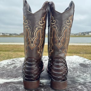 Pu&ograve; includere: Un paio di stivali da cowboy in pelle marrone con motivo a pelle di serpente e ricami intricati sullo stivale.