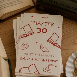 Puede incluir: Una pila de tarjetas de cumpleaños rectangulares de color blanco roto con ilustraciones de líneas rojas de libros abiertos, un aguacate, una rodaja de sandía y cerezas. El texto dice CHAPTER 30, THE STORY CONTINUES... EMILY'S 30TH BIRTHDAY, con estrellas rojas.