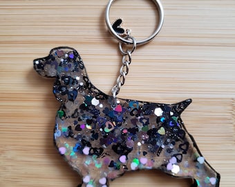Może przedstawiać: Brelok do kluczy z czarnej i srebrnej żywicy w kształcie koker spaniel. Brelok ma srebrny metalowy pierścień i łańcuszek.