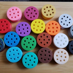 May include: A collection of 18 colourful round discs with star-shaped holes. Each disc is a different colour, including red, blue, green, yellow, orange, purple, brown, black, white, and grey.