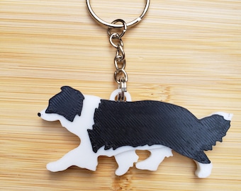 Może przedstawiać: Brelok do kluczy w kształcie czarno-białego border collie. Brelok jest wykonany z plastiku i ma srebrny metalowy pierścień.