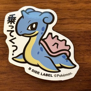 May include: A blue and yellow cartoon sticker of a Pokemon character with a pink shell on its back. The sticker has Japanese text that says "来てる?" and the text "B Side Label ©Pokémon."