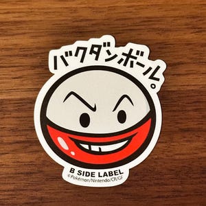 Puede incluir: Una pegatina blanca y roja con una cara de dibujos animados y el texto "B SIDE LABEL" y "Pokémon/Nintendo/CR/GF". La cara de dibujos animados tiene una boca roja con dientes blancos y ojos negros. El texto "B SIDE LABEL" está en negro y el texto "Pokémon/Nintendo/CR/GF" está en negro más pequeño.