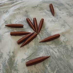 Peut inclure: Dix objets bruns en forme de balles, avec des pointes, sont disposés sur un tissu clair à motifs. Les objets semblent être en bois ou dans un matériau similaire. Disposition en cercle.