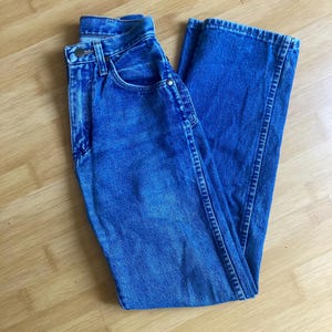 May include: A pair of medium-wash blue denim jeans featuring a high-waisted design, a classic button and zip fly closure, belt loops, and traditional five-pocket styling with metal rivets and visible stitching along the seams.