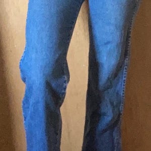 May include: High-waisted blue denim jeans featuring a classic five-pocket design, a metal button closure at the waistband, and a straight-leg cut. The denim has a medium blue wash with subtle fading along the thighs and seams, finished with a standard hem.